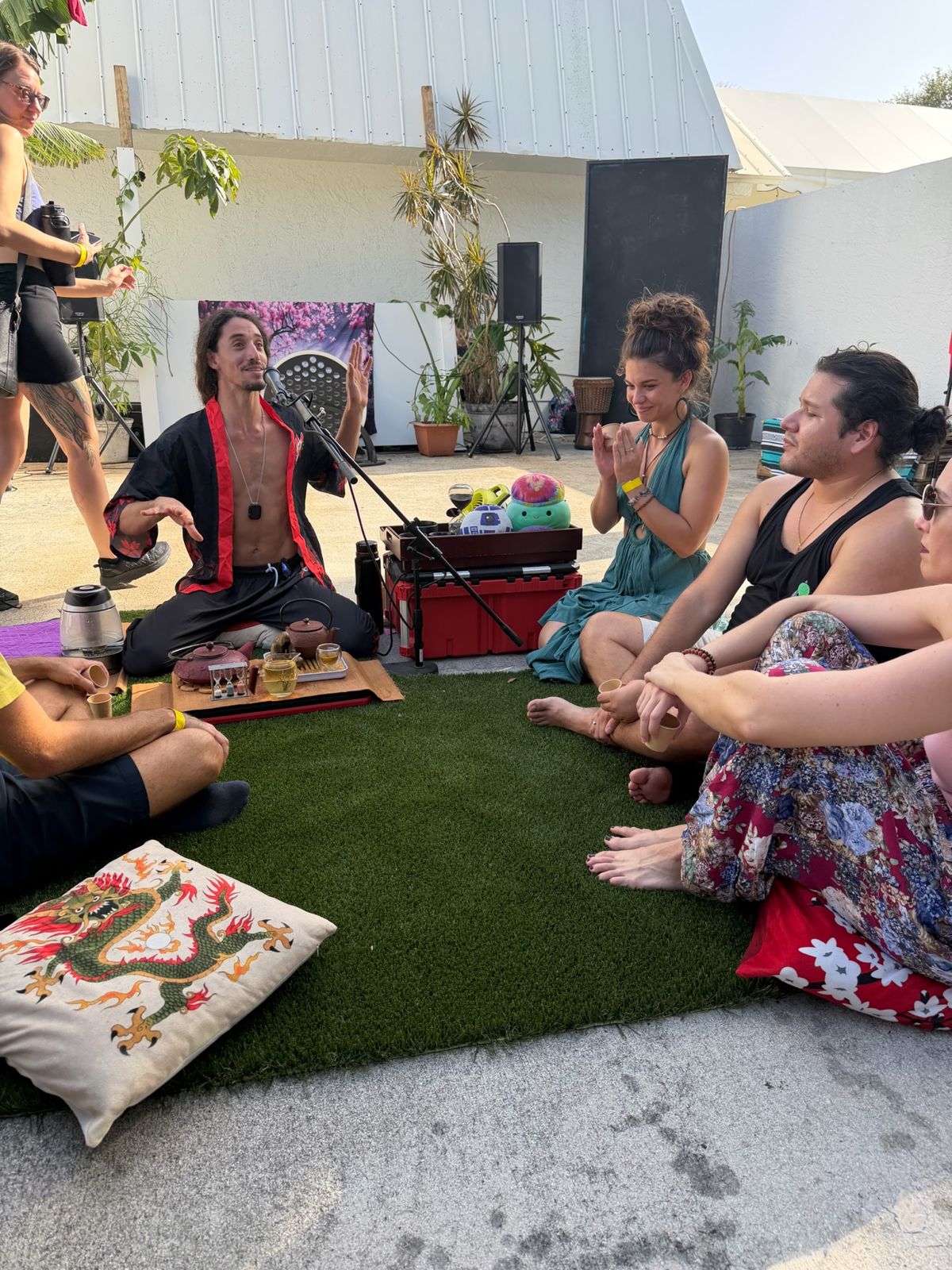 Jake teaching a circle of people sitting on the grass around a tea table