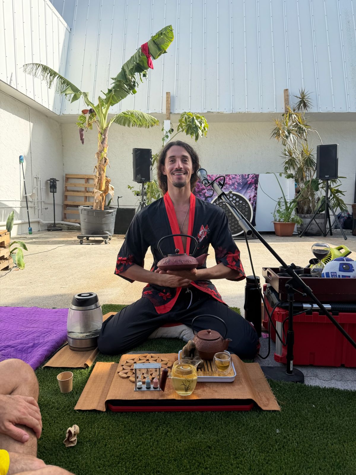 Jake seated cross-legged behind a tea set, smiling