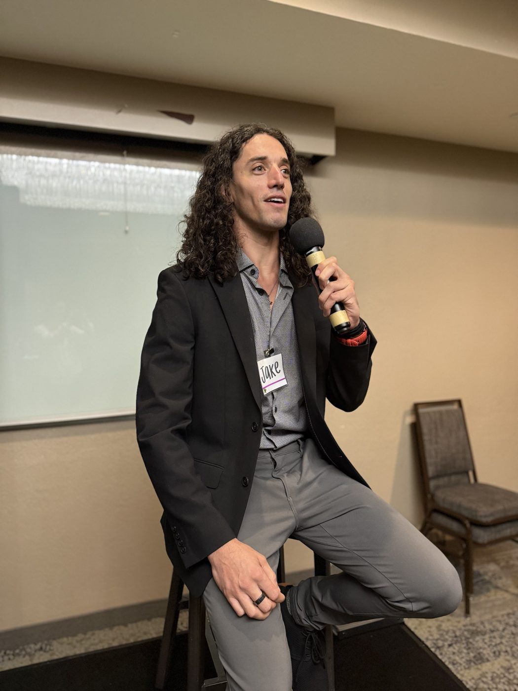 Jake on stage on a stool with a microphone, mid-sentence